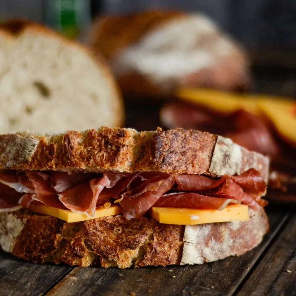 Deli sandwich with cured ham and cheese on toasted sourdough on a wooden board