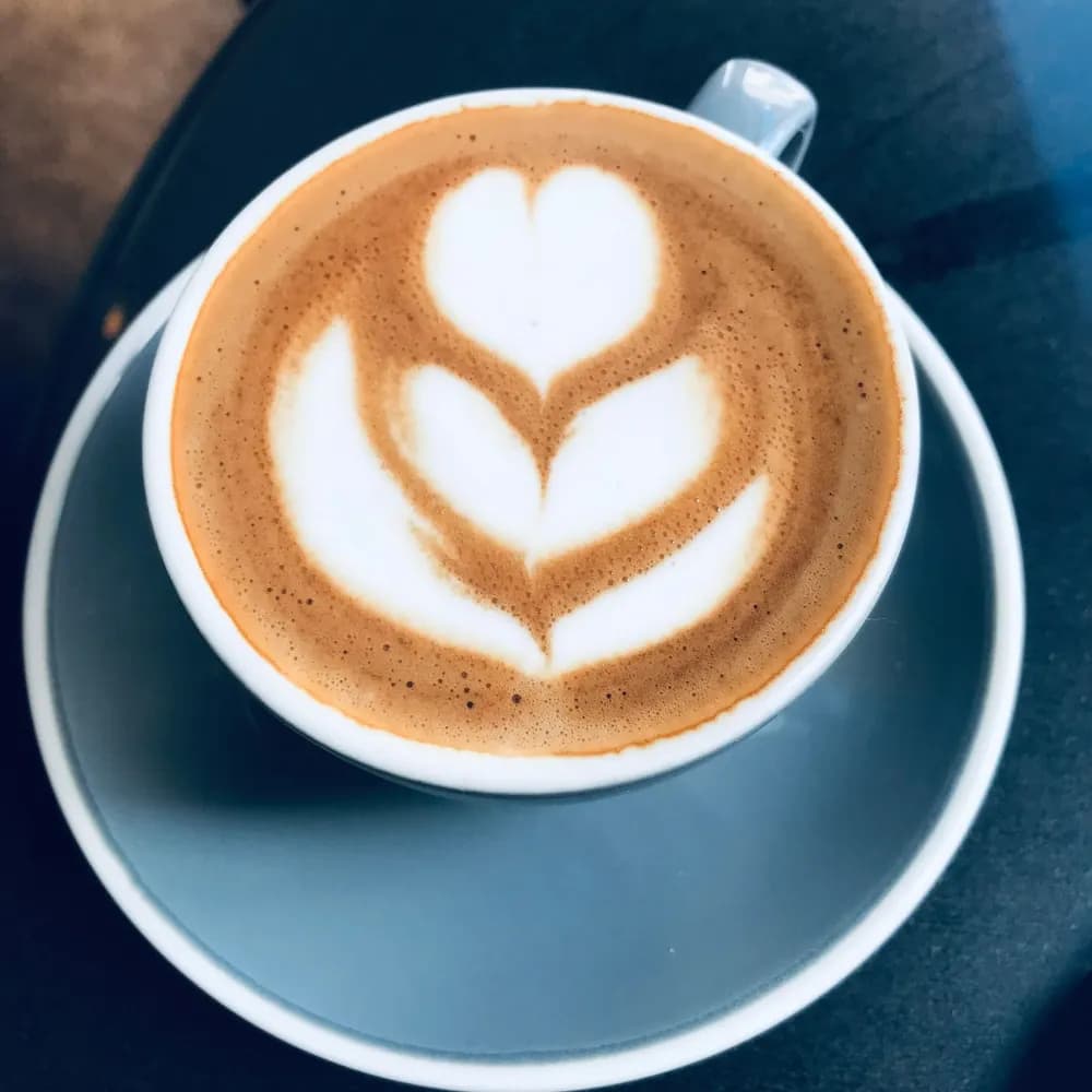 Latte with leaf-shaped latte art in a blue cup and saucer